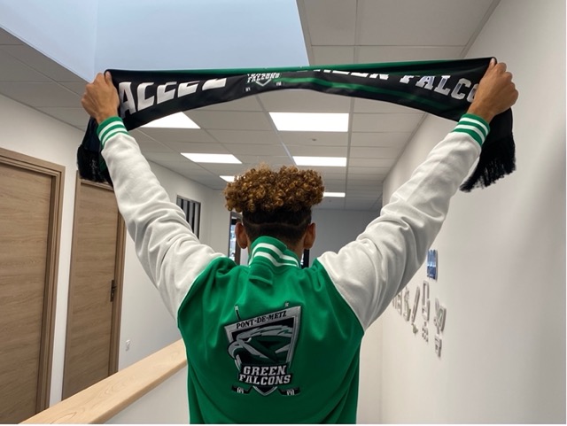 une personne de dos portant une veste verte du club Green Falcon et qui brandit en l'air une écharpe de suppporter
